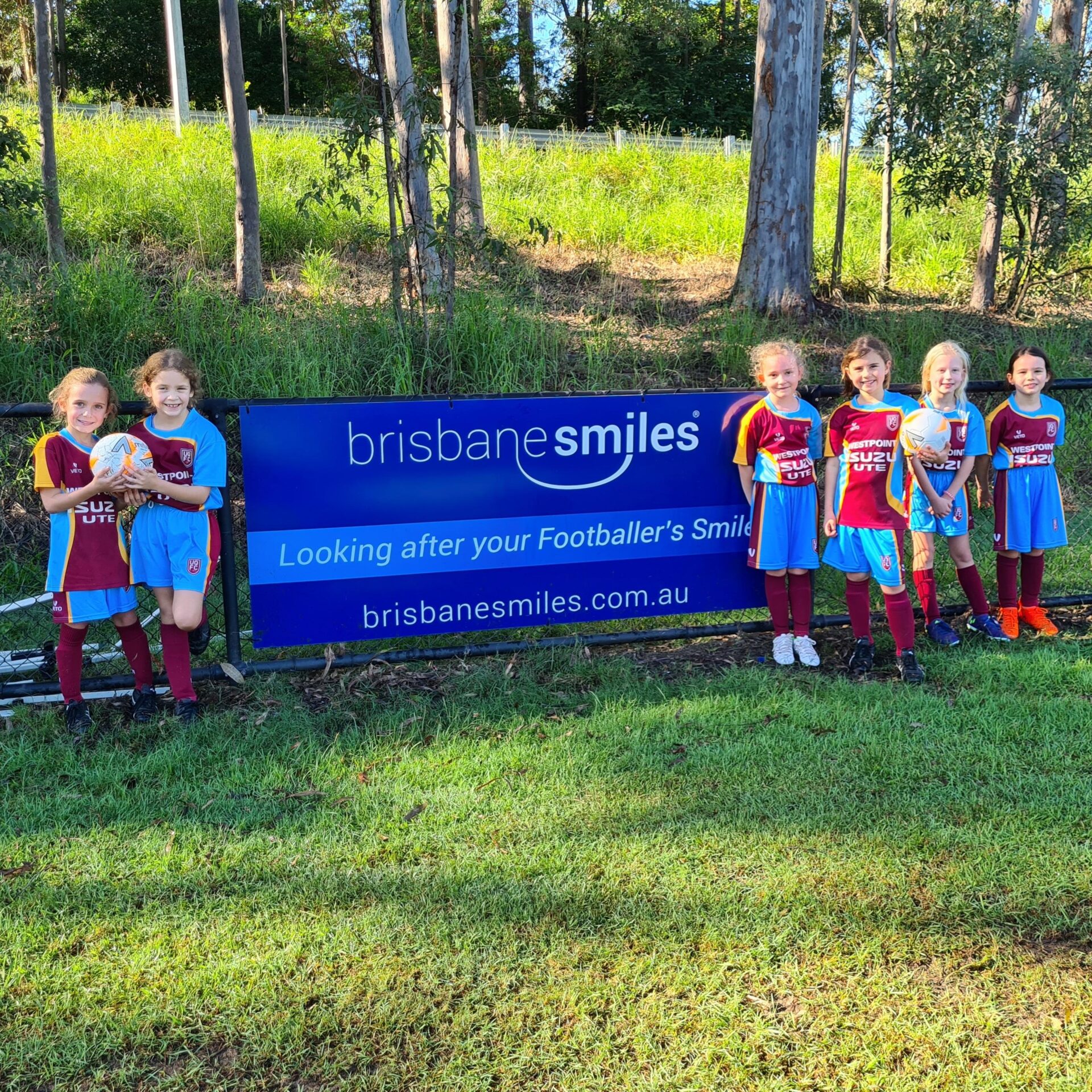Children next to Brisbane Smiles banner on a football field at UQFC